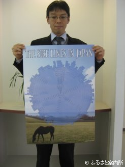 完成したポスターを手にする事務局の山内さん。ポスターでは下で紹介した種牡馬のサイアーラインが一目でわかる